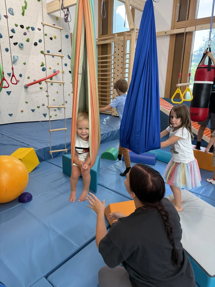 Betreuerin und Kinder an der Kletterwand mit blauem Schwungtuch im ANKERZEIT-Freiraum