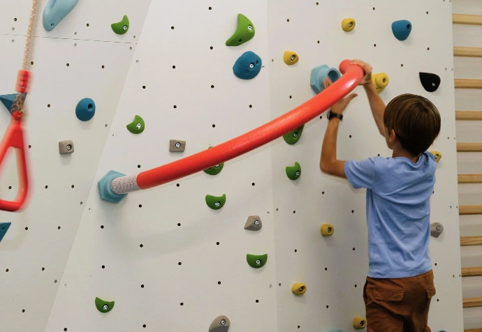 Kind hält sich an einem roten Ring an der Boulderwand fest im ANKERZEIT-Freiraum