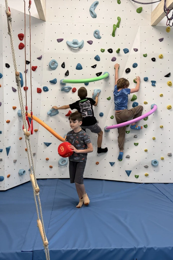 Kinder klettern an der Boulderwand, ein Kind schwingt am Seil im ANKERZEIT-Freiraum
