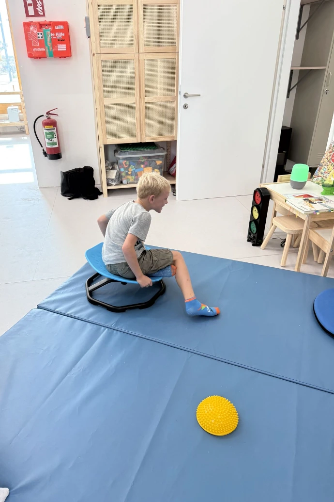 Kind sitzt auf einer blauen Matte neben einem gelben Stein im ANKERZEIT-Freiraum