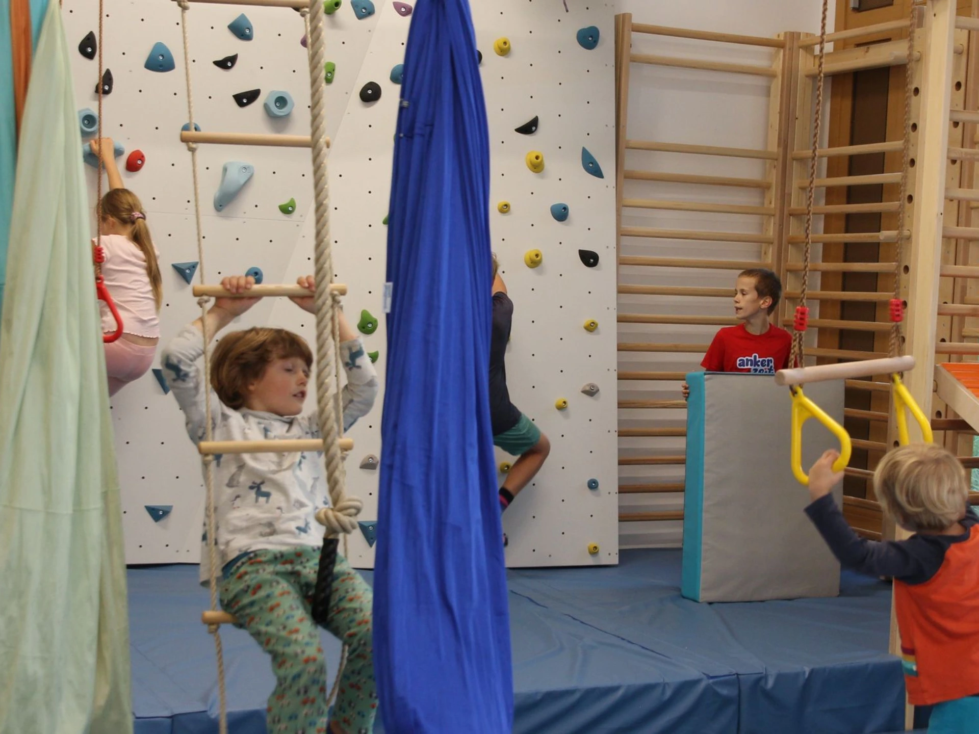 Kinder klettern und schaukeln an einer Strickleiter vor der Kletterwand im Freiraum von ANKERZEIT