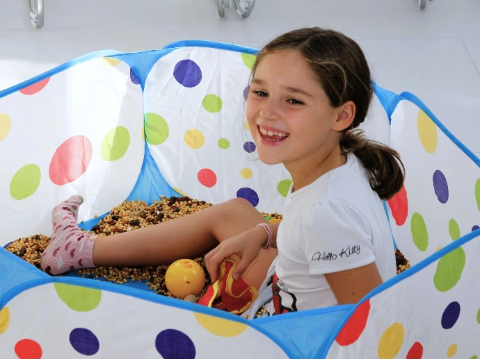 Lachendes Mädchen sitzt mit Bällen in einem bunten Spielzelt